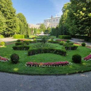 Man sieht einen runden Weg im Wiener Volksgarten. Im Zentrum eine Grüninsel mit Blumen.